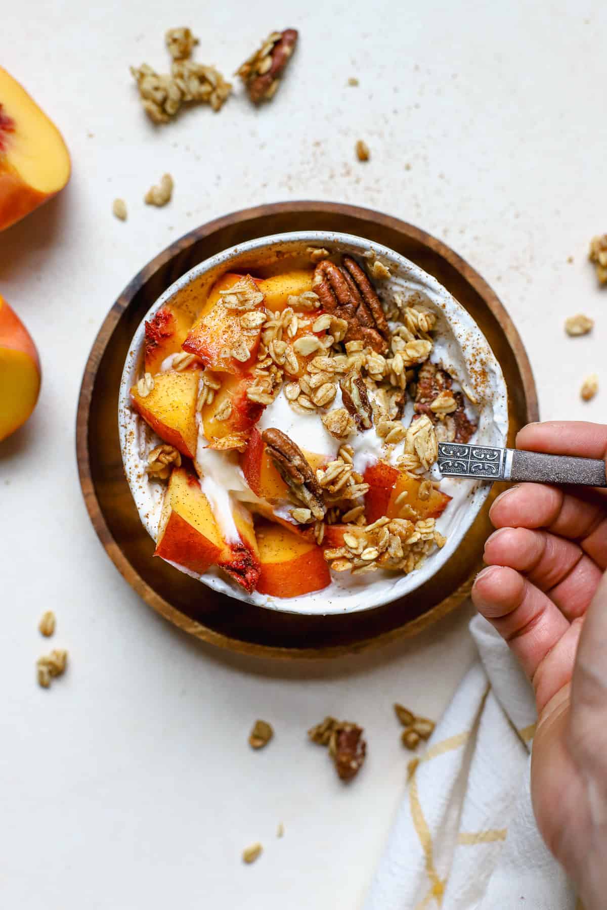 Fresh peach pie yogurt bowl in small white bowl with hand holding spoon and taking a scoop.
