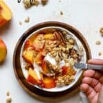 Peach pie yogurt bowl with granola and hand scooping a spoonful of yogurt.