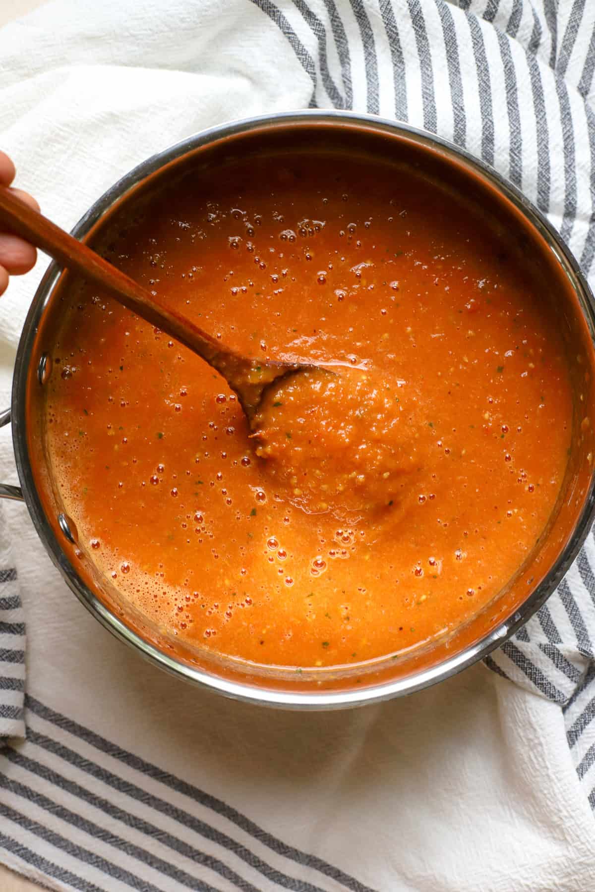 Roasted tomato soup in stainless steel pot being stirred with wooden spoon.