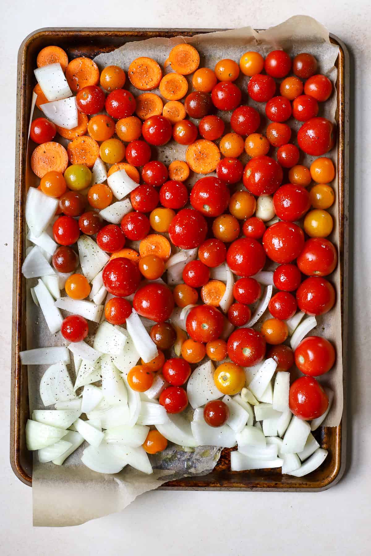 Seasoned tomatoes, onions, carrots, and garlic on sheet pan.