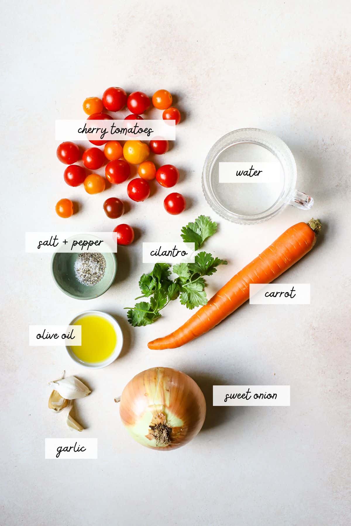 Roasted cherry tomato soup ingredients, including cherry tomatoes, carrot, onion, garlic, water, cilantro, salt + pepper, and olive oil.