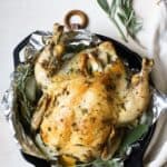 Simple whole roasted chicken with herbs in cast iron skillet.