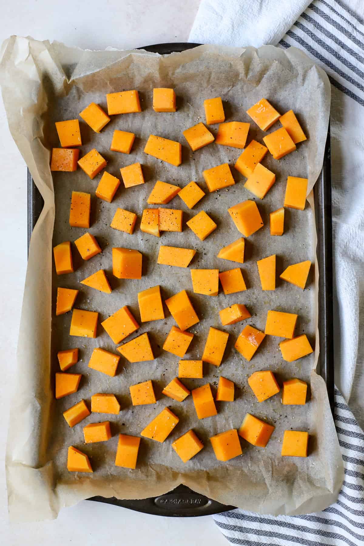 Seasoned butternut squash cubes on sheet pan before roasting.