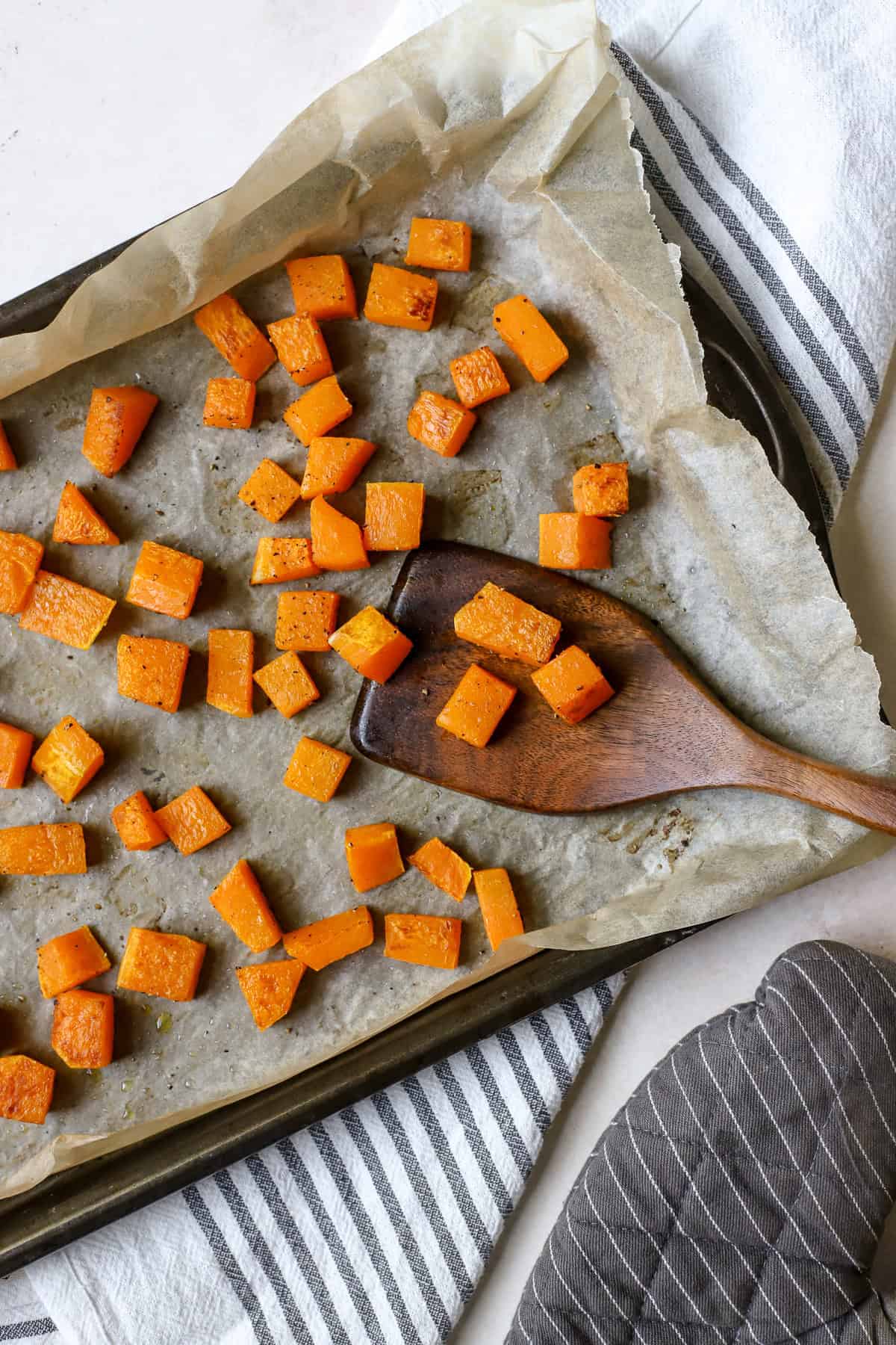 Roasted butternut squash cubes on sheet pan with wooden turner.