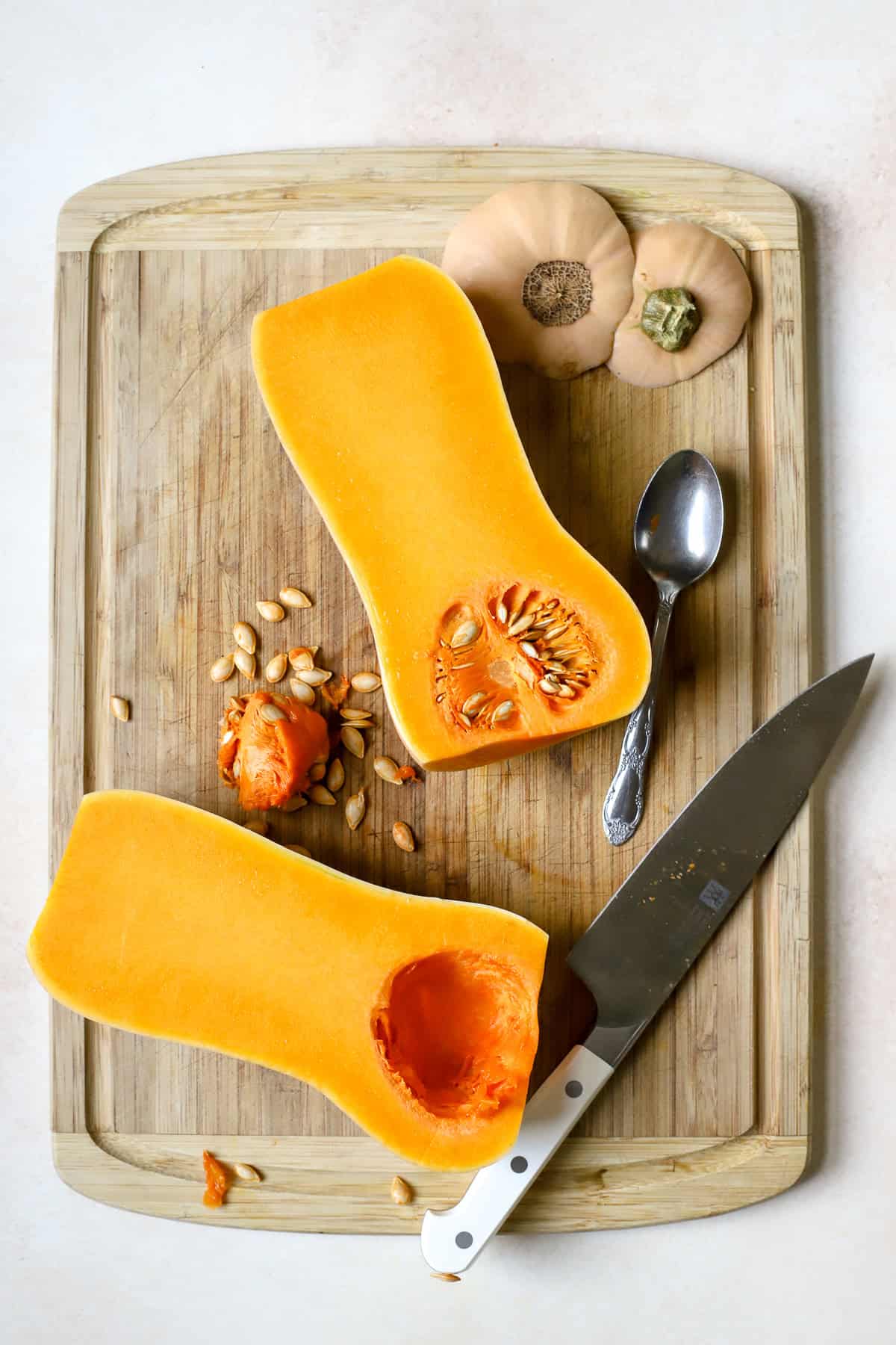 Scooping seeds out of halved butternut squash.