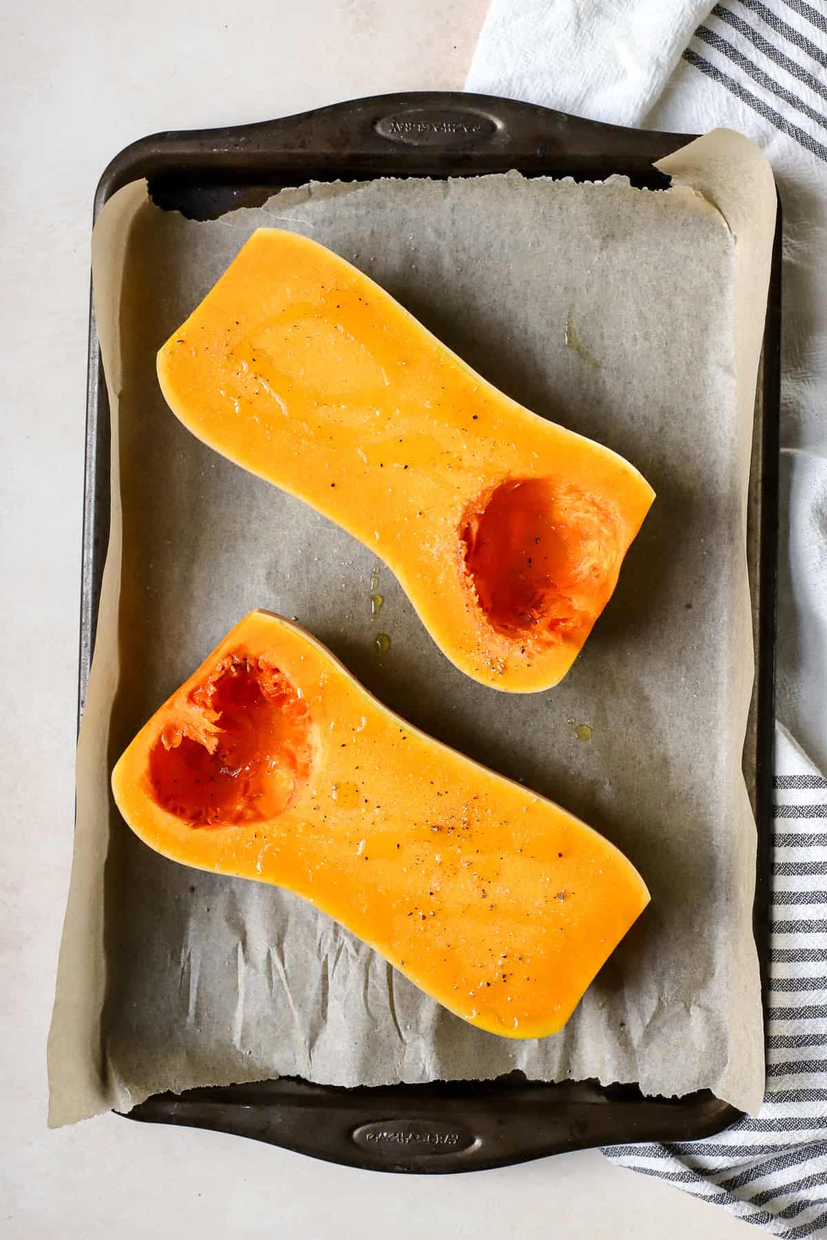 Seasoned butternut squash halves on sheet pan before roasting.