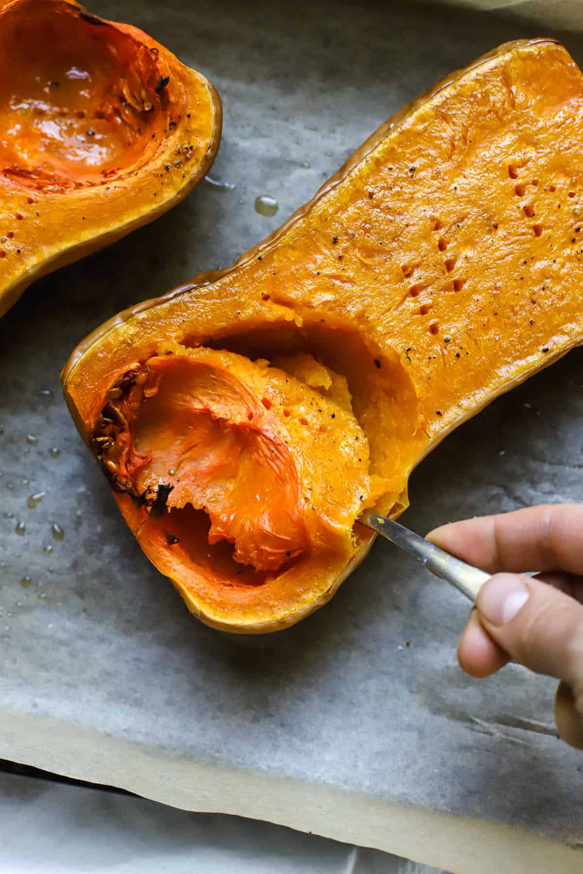 Roasted butternut squash half with spoon scooping out the soft roasted squash.