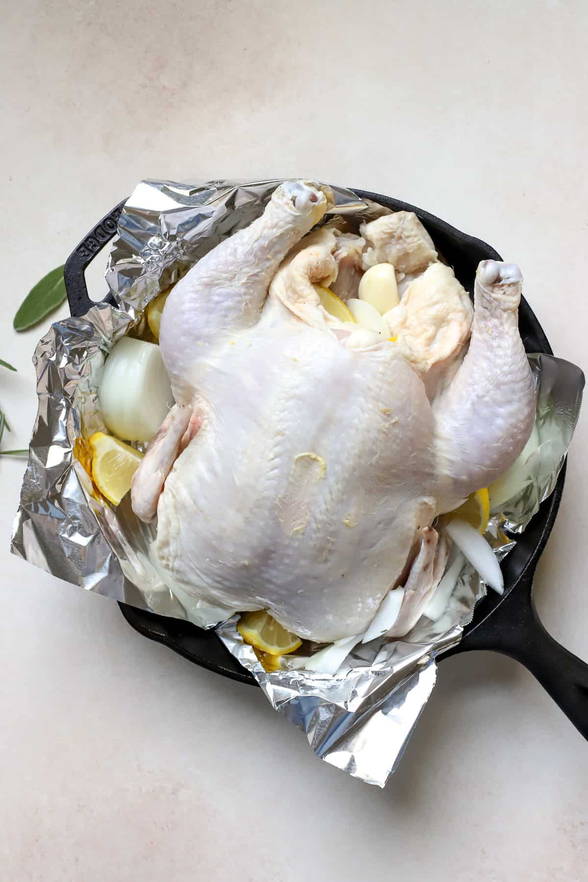 Whole raw chicken in foil-lined cast iron skillet.