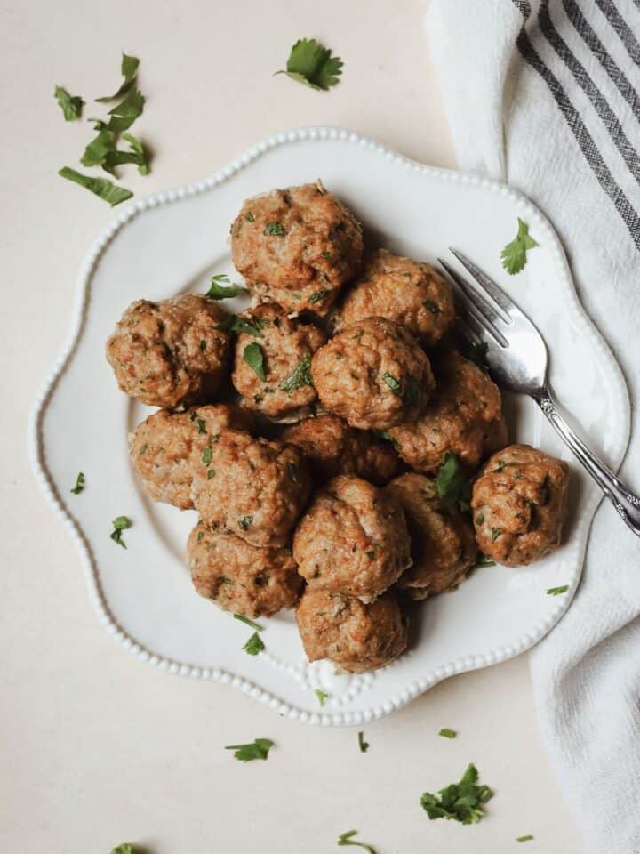 Baked turkey meatballs piled onto a white plate with fork.