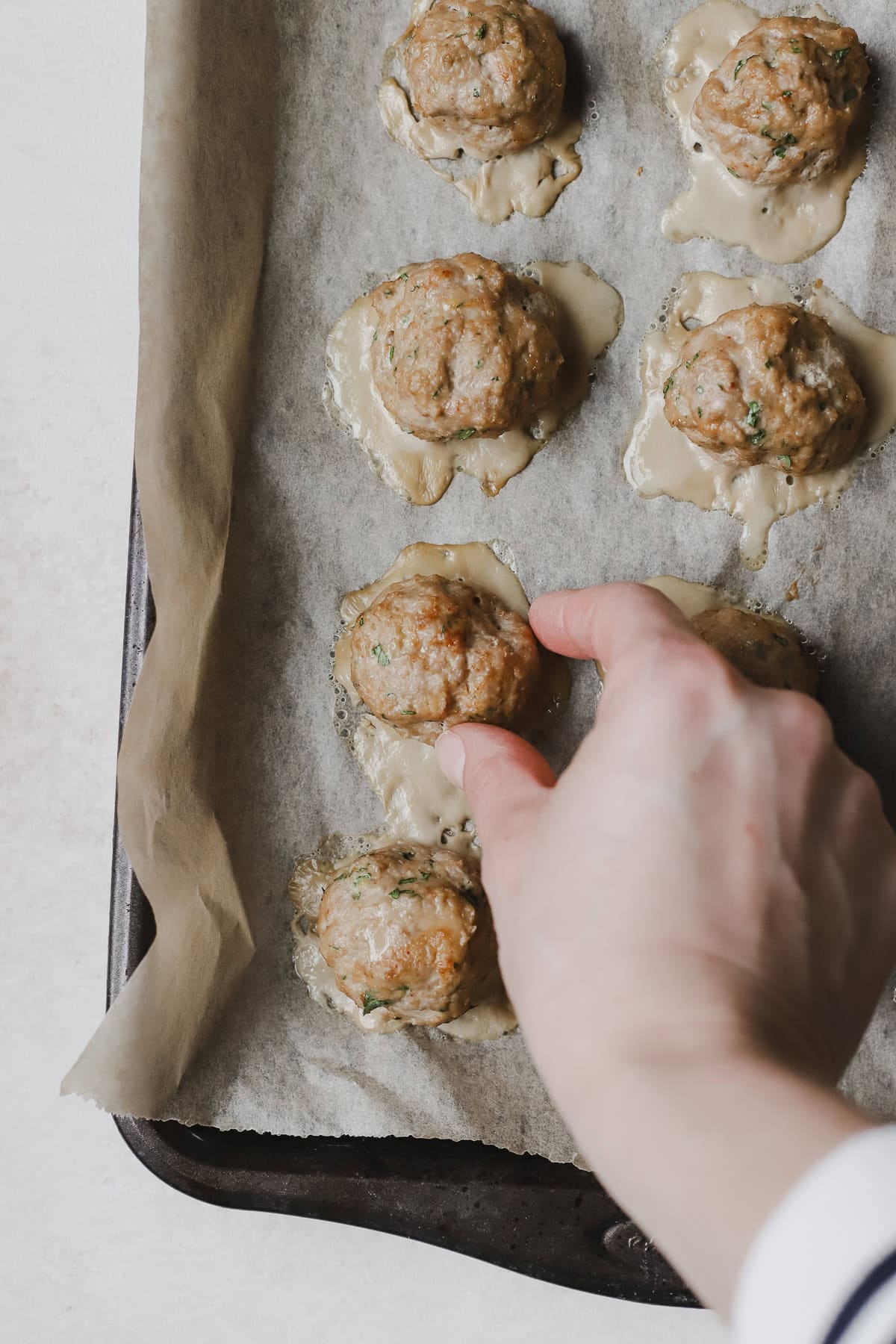 Hand picking up a turkey meatball from sheet pan.
