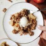 A scoop of healthy apple crisp with vanilla ice cream on dessert plate with fork.