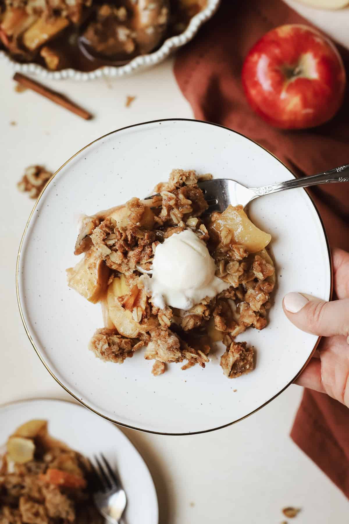 A scoop of healthy apple crisp with vanilla ice cream on dessert plate with fork.