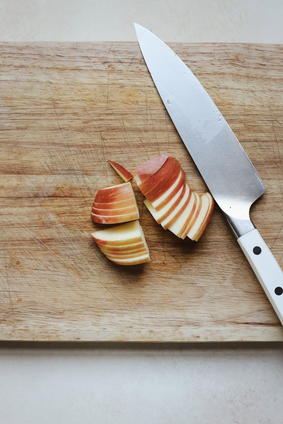 Thinly sliced apples on cutting board with chef's knife.