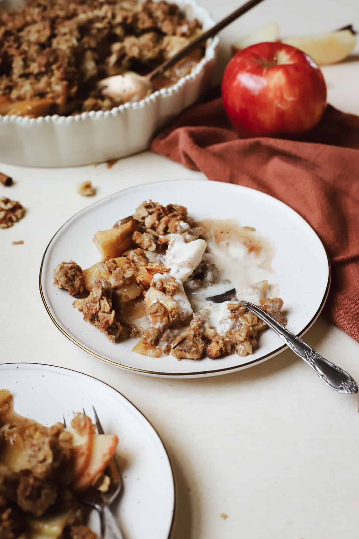 Scoop of apple crisp on small cream colored plate with fork.