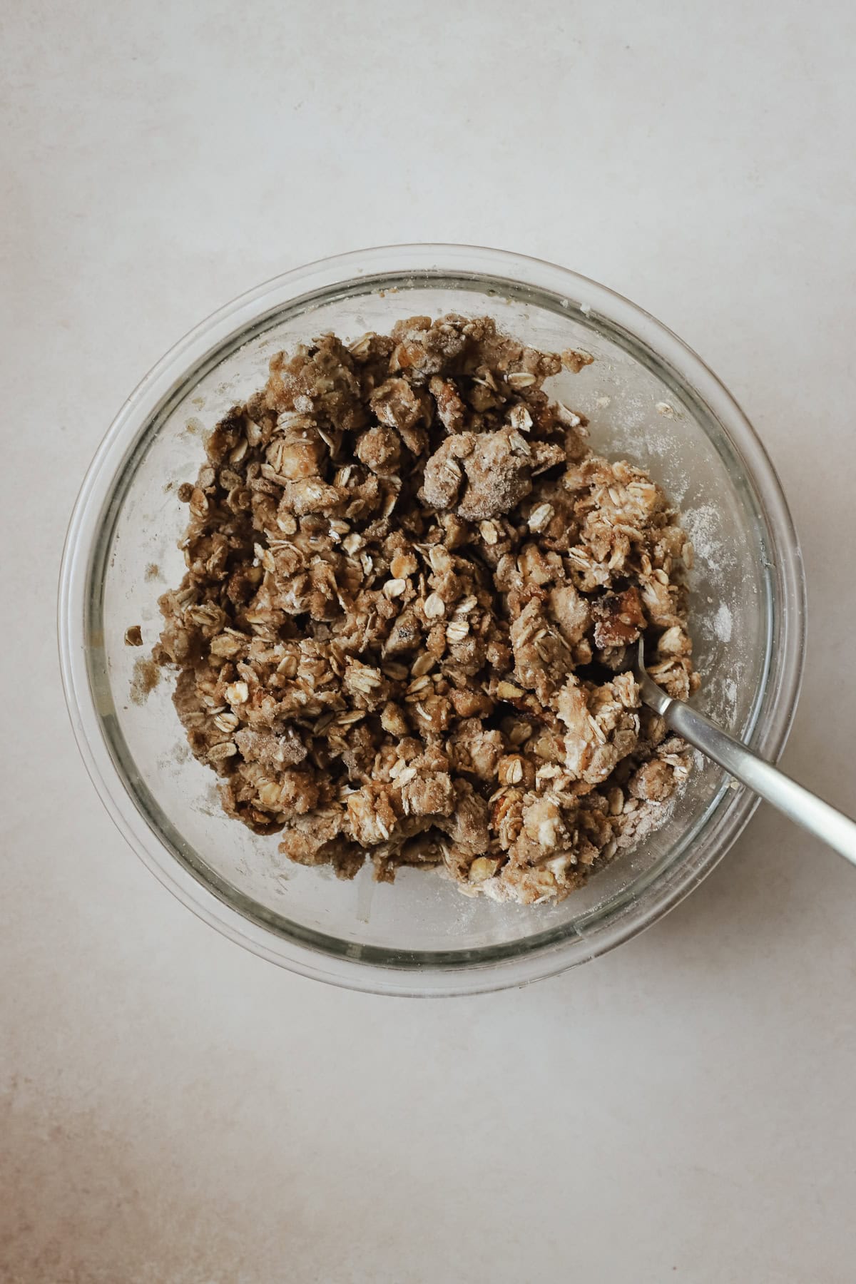 Apple crisp topping ingredients in clear glass bowl with fork.