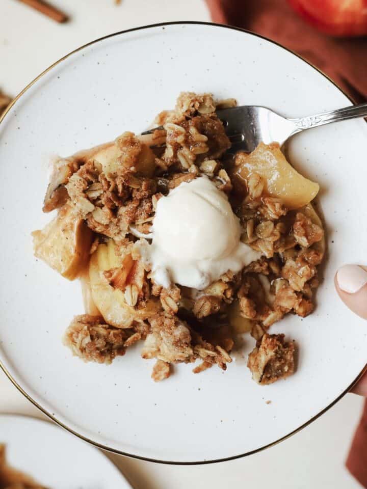 A scoop of healthy apple crisp with vanilla ice cream on dessert plate with fork.