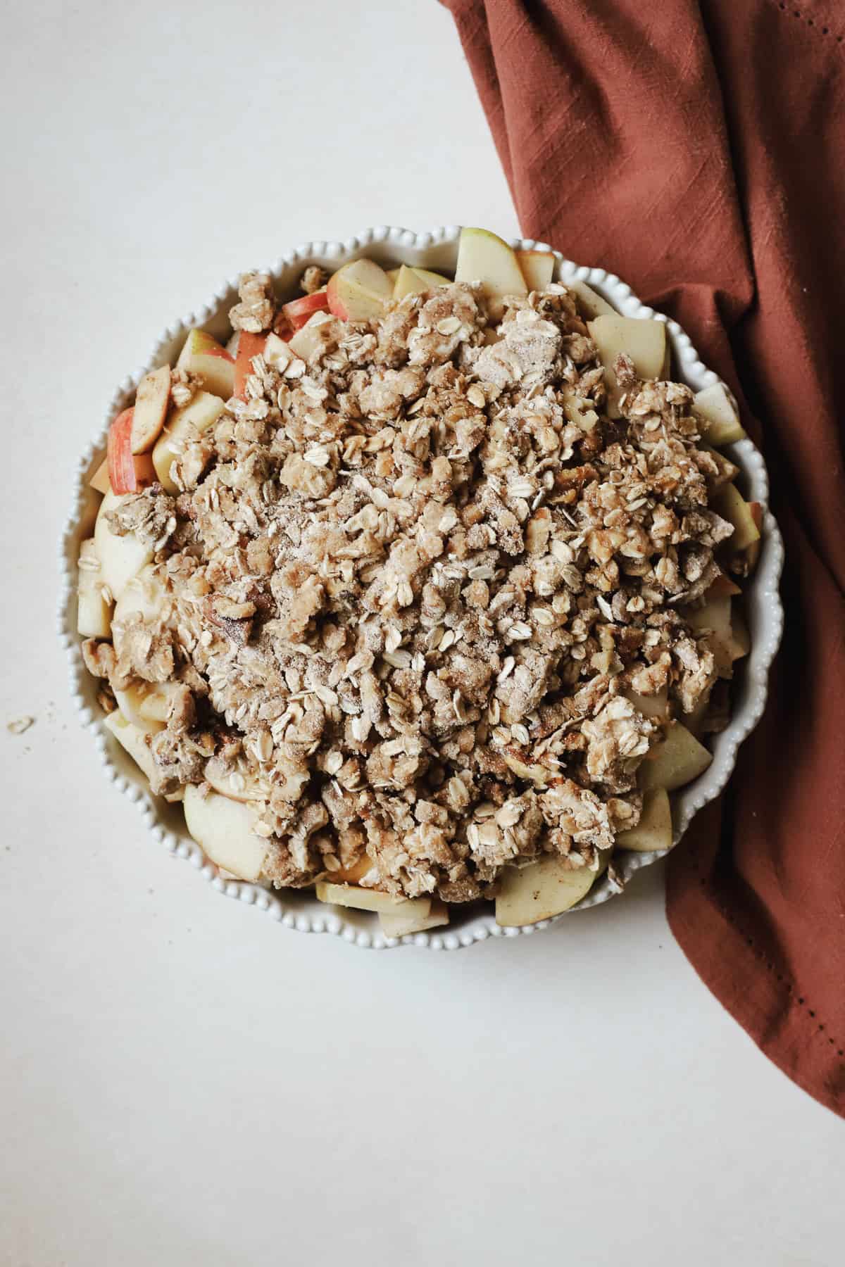 Apple crisp filling and topping in prepared ceramic pie dish, ready to be baked.