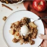 A scoop of healthy apple crisp with vanilla ice cream on dessert plate with fork.