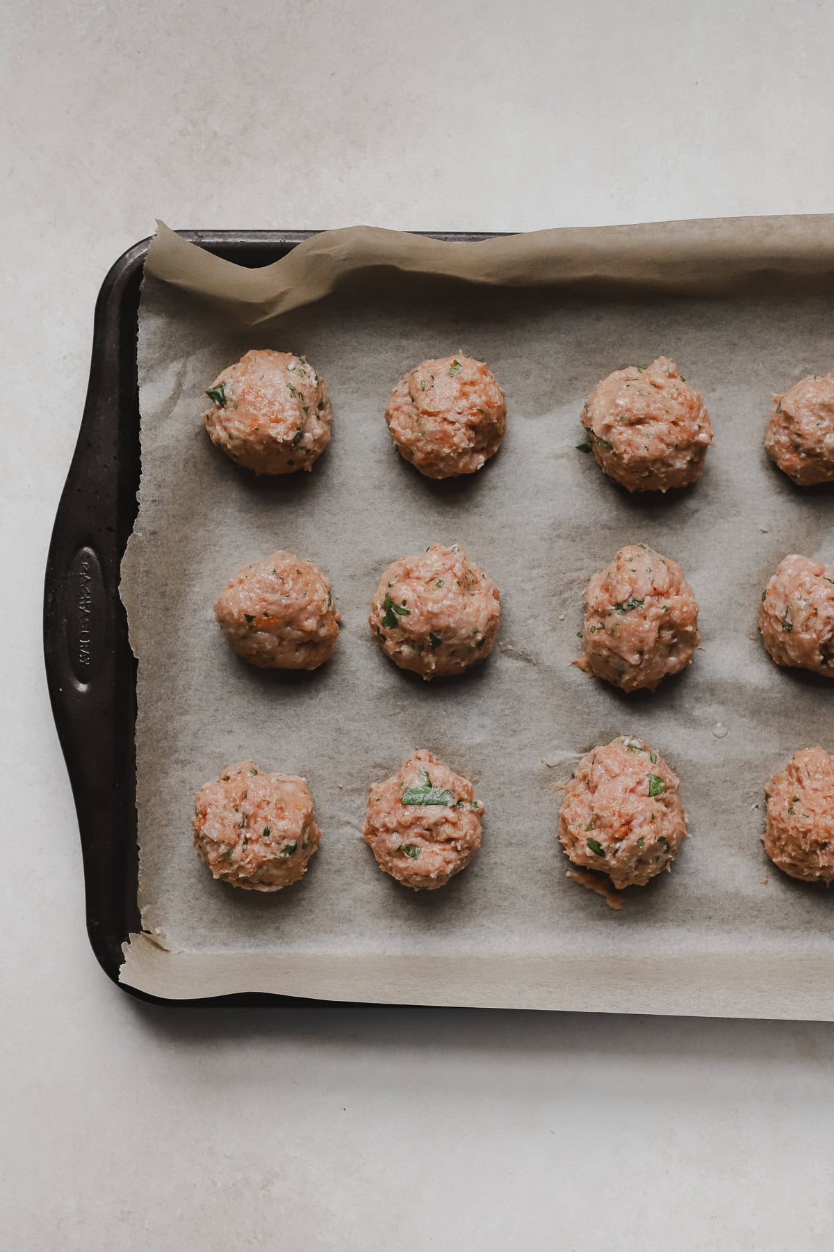 Raw turkey meatballs lined up on baking sheet.
