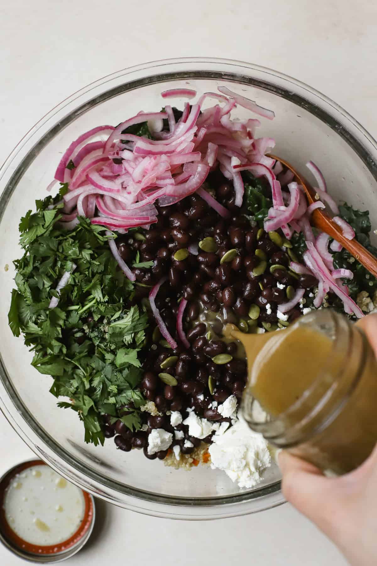 Pouring cumin orange vinaigrette onto quinoa salad in a bowl.