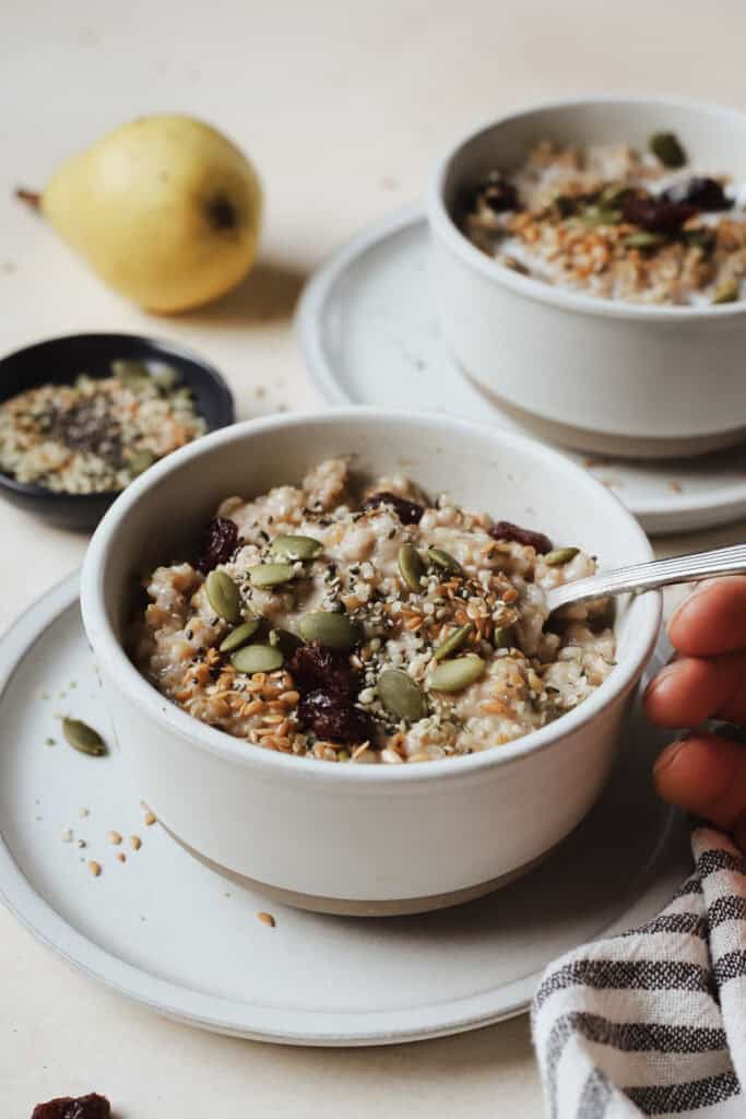 Bowl of steel cut oats on small plate with hand holding spoon.