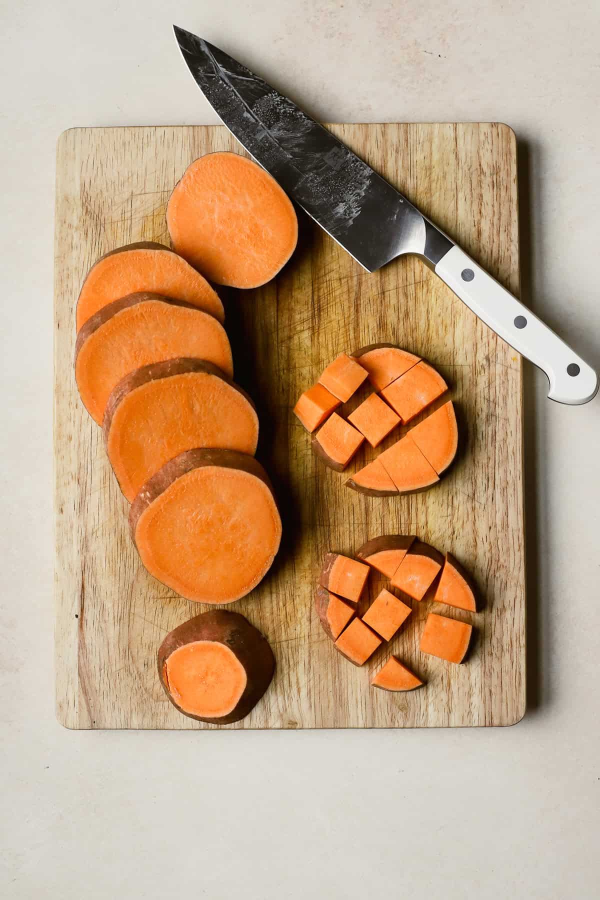 Sweet potato medallions and cubes on cutting board with chef's knife.