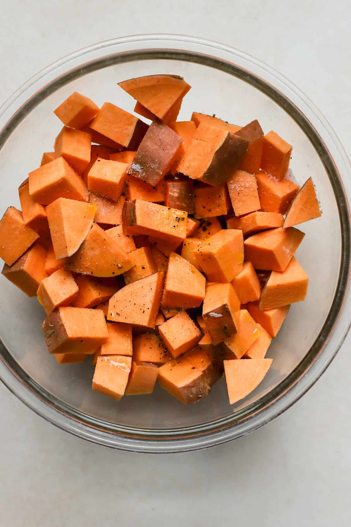 Seasoned and cubed sweet potatoes in clear glass bowl.