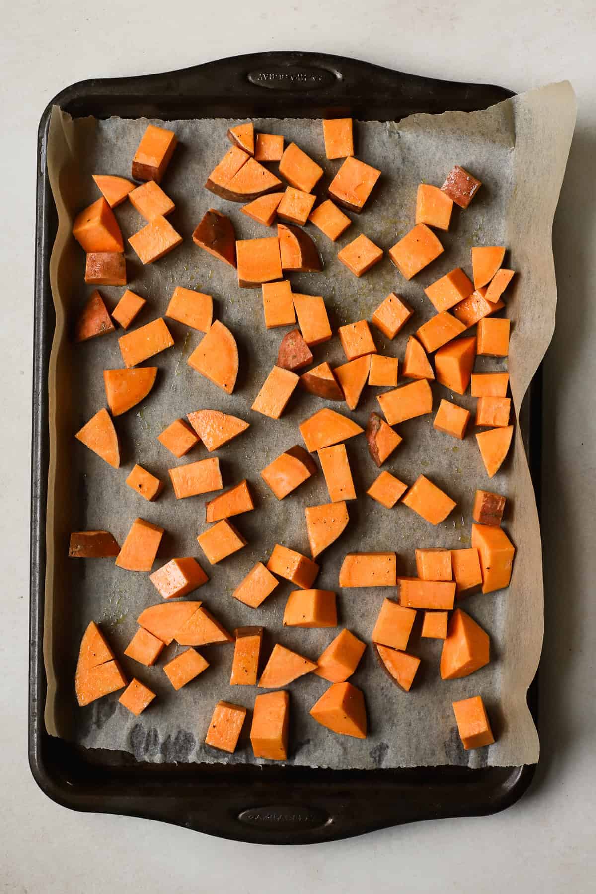 Seasoned and cubed sweet potatoes on parchment-lined sheet pan.