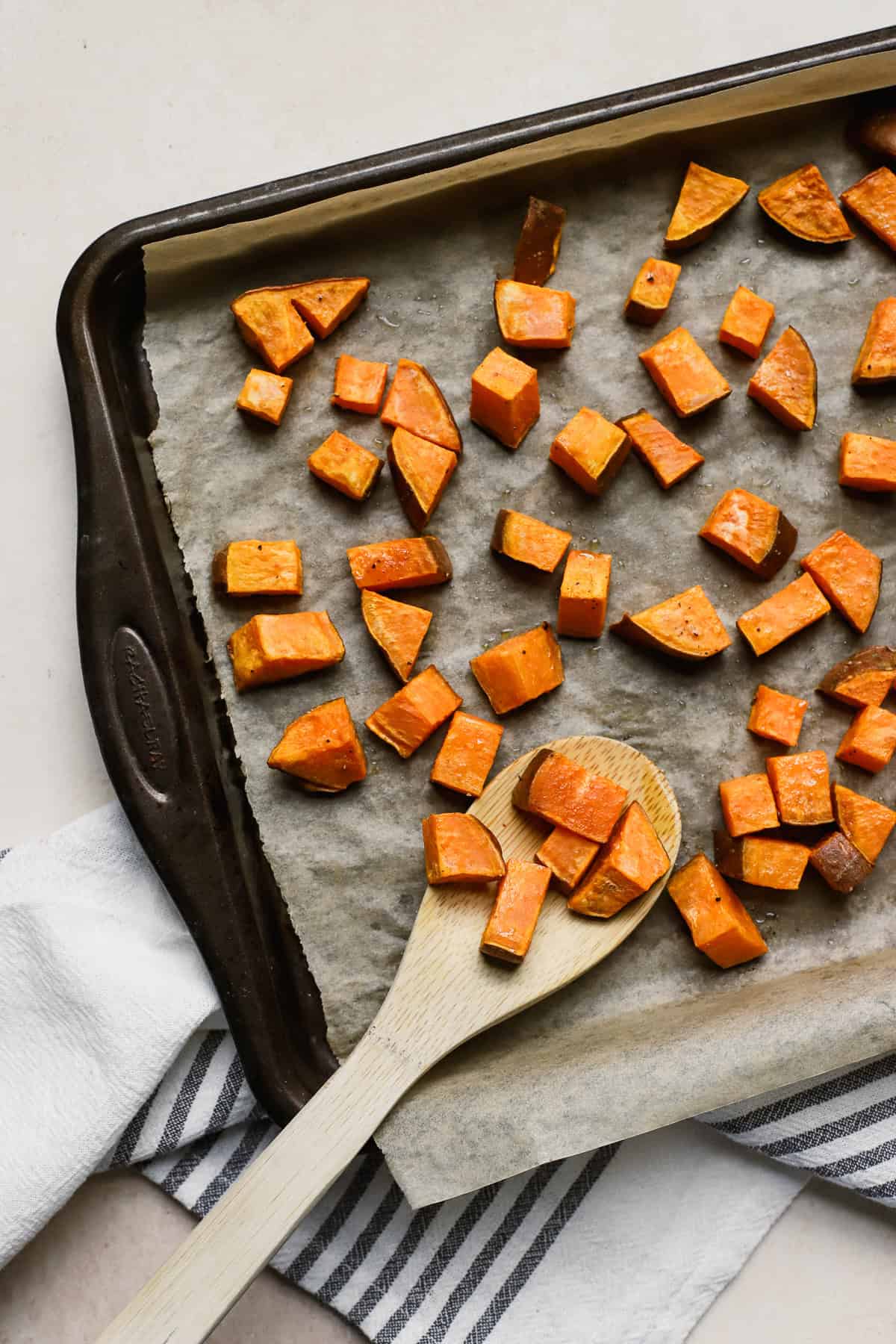 Roasted sweet potatoes on sheet pan with bamboo serving spoon.
