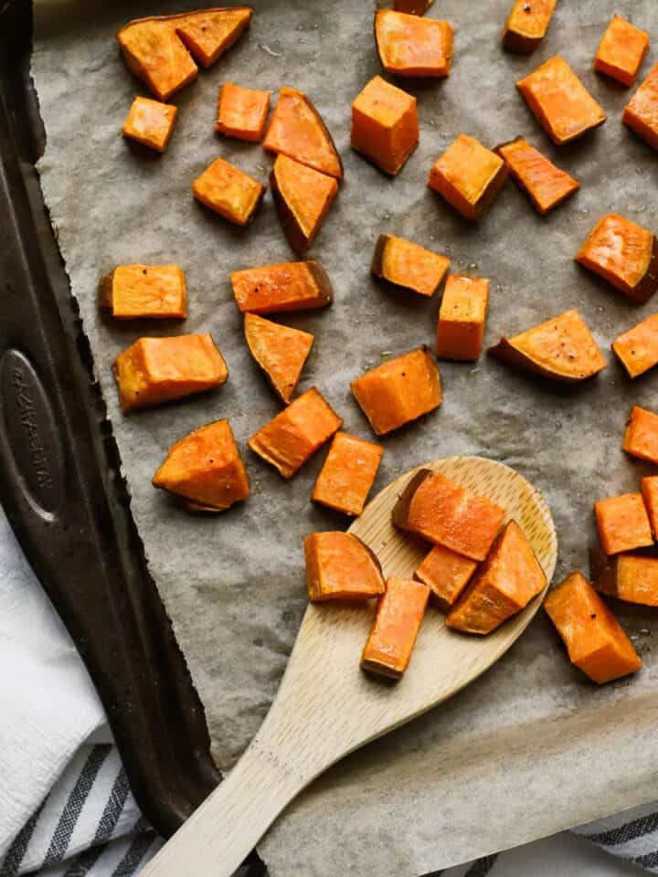 Roasted sweet potatoes on sheet pan with bamboo serving spoon.
