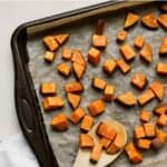 Roasted sweet potatoes on sheet pan with bamboo serving spoon.