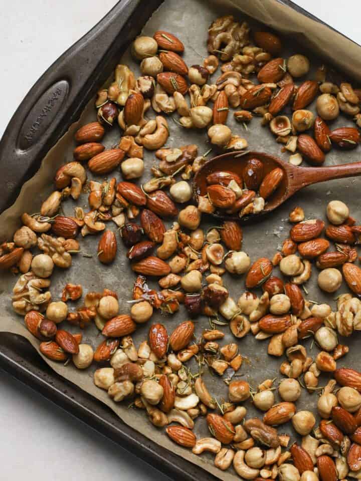 Roasted rosemary nuts on sheet pan with wooden spoon.