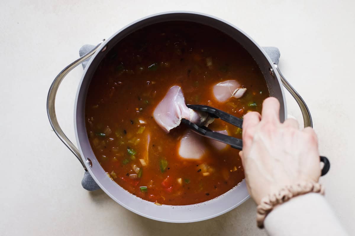 Add chicken thighs to tomato broth for tortilla soup.