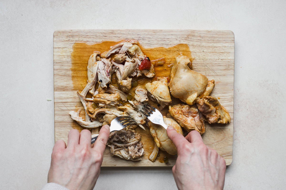 Shredded chicken thighs on cutting board.