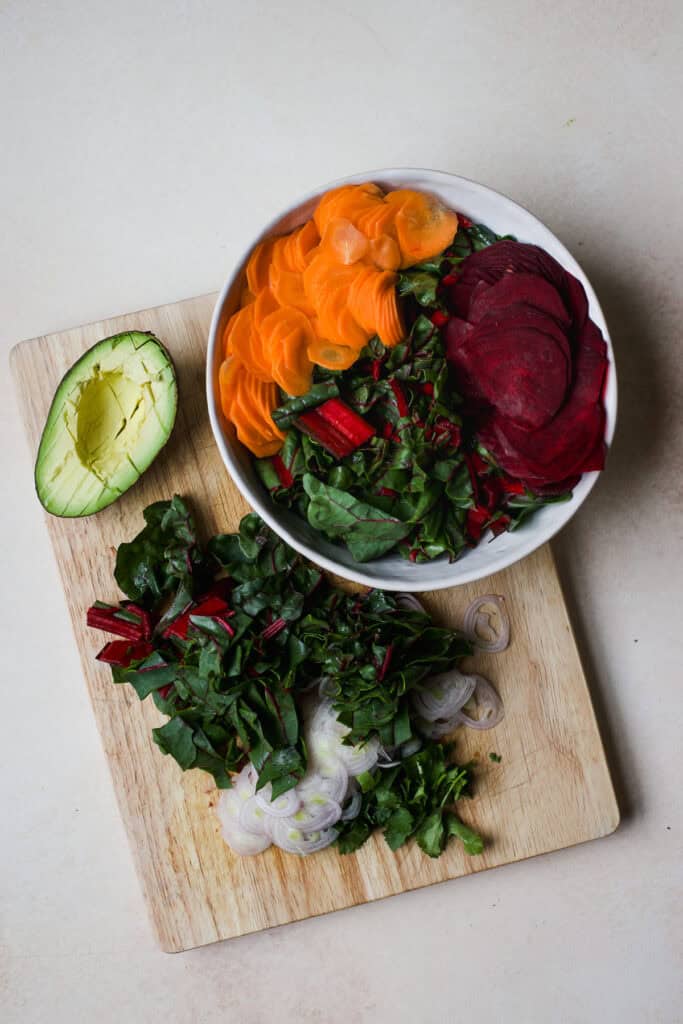 Prepped greens, beet and carrot salad ingredients on bamboo cutting board.