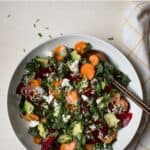 Greens salad with beets and carrots in large white serving bowl with serving spoons.
