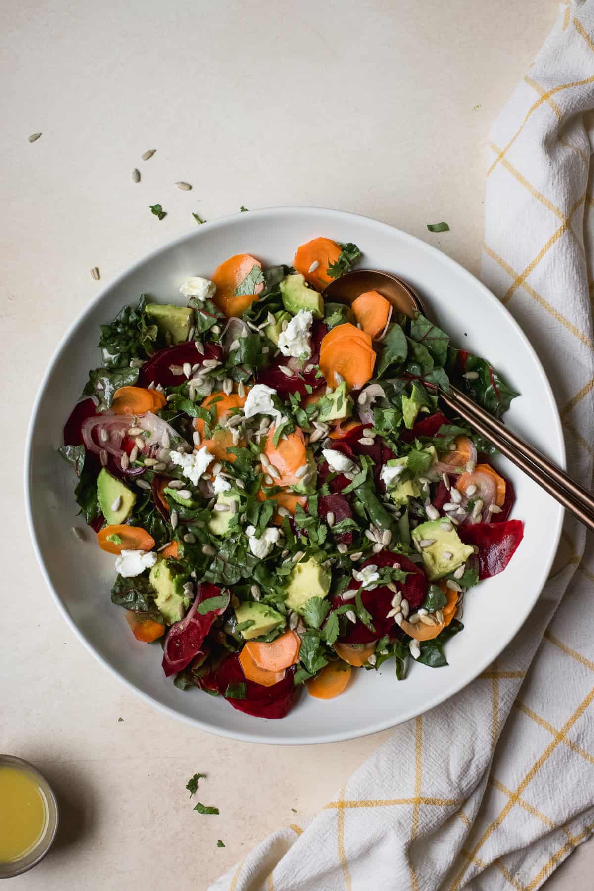 Greens salad with beets and carrots in large white serving bowl with serving spoons.