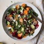 Greens salad with beets and carrots in large white serving bowl with serving spoons.