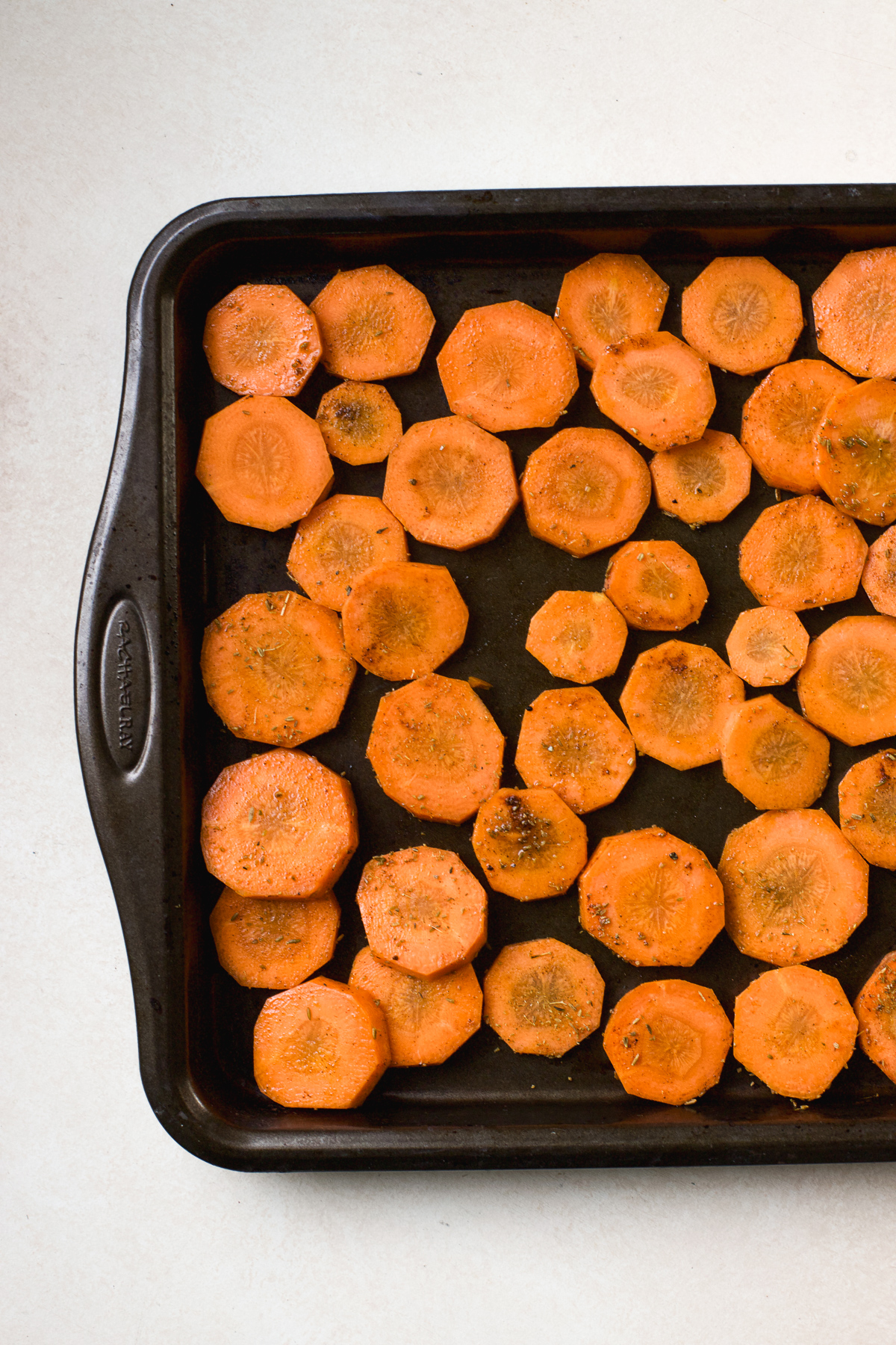 Seasoned carrot slices in a single layer on sheet pan.