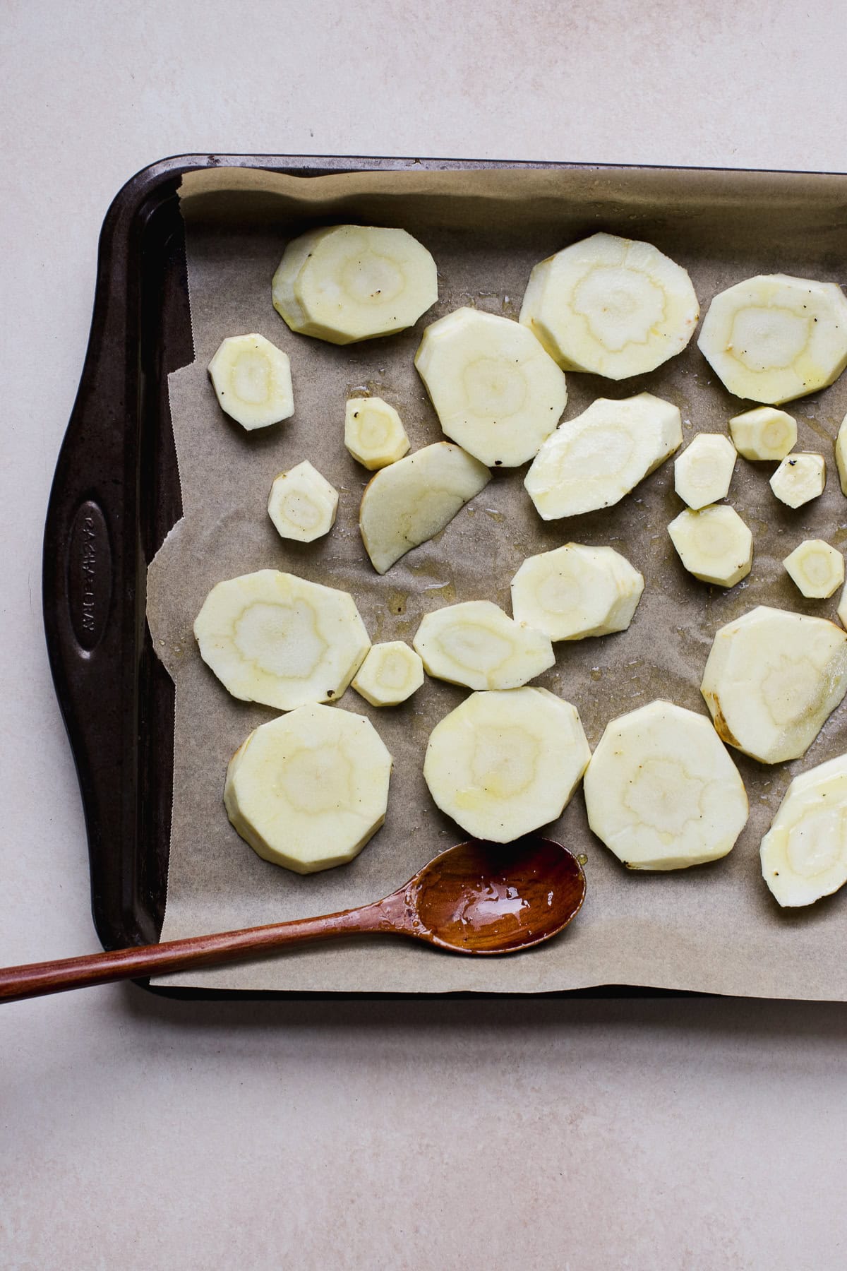 Seasoned parsnip slices on sheet pan before roasting.
