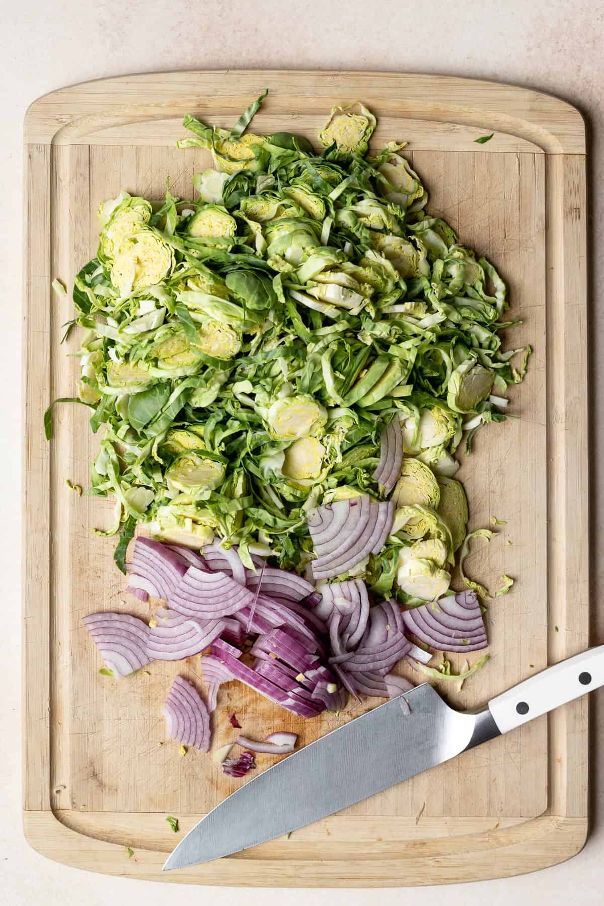 Chopped Brussels sprouts and sliced red onions on a large bamboo cutting board.
