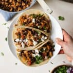 Hand holding a plate of three ground chicken tacos.