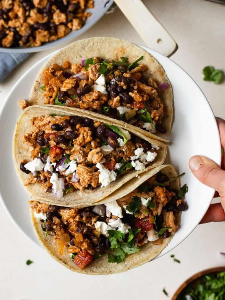 Hand holding a plate of three ground chicken tacos.