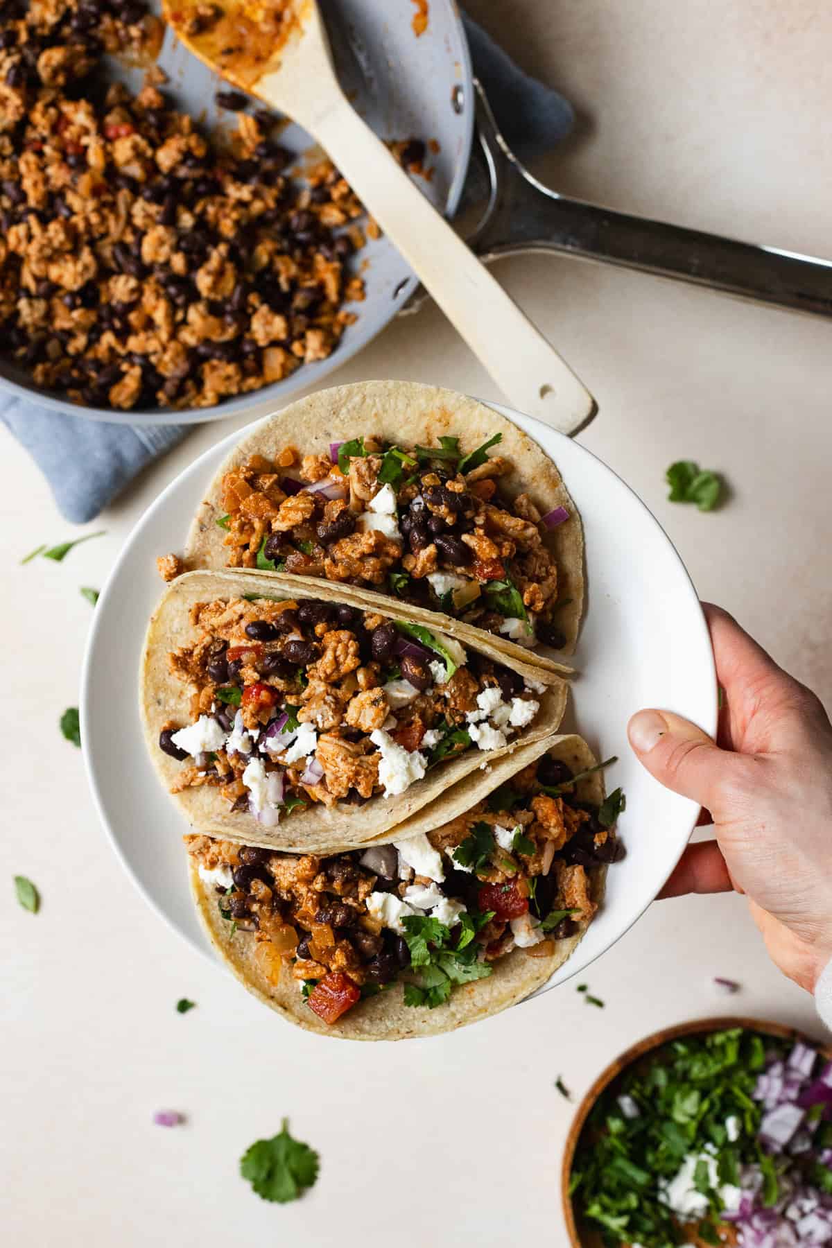 Hand holding a plate of three ground chicken tacos.