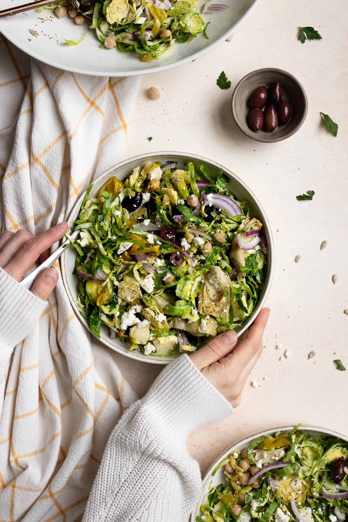 Hands around bowl of chopped Brussels sprouts salad.