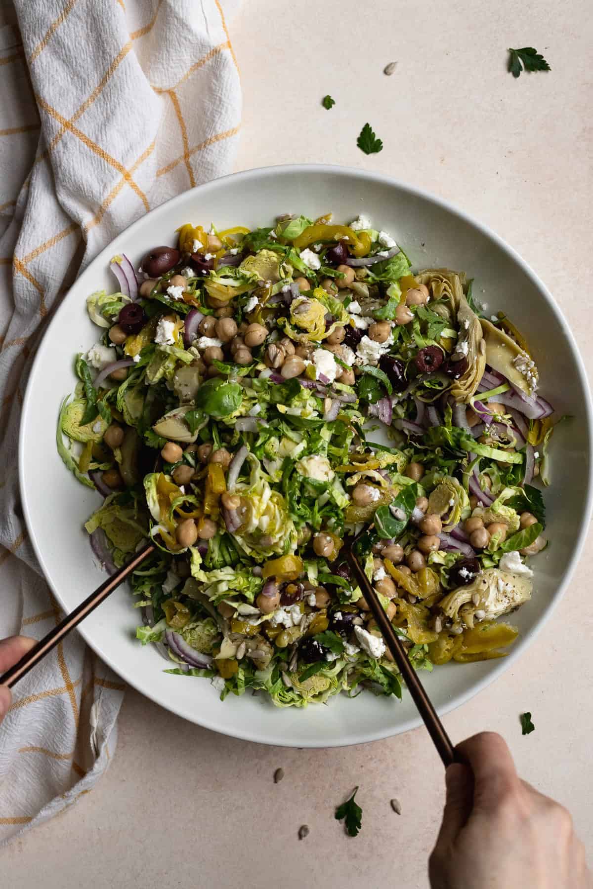 Tossing Brussels sprouts chopped salad in large white serving bowl.