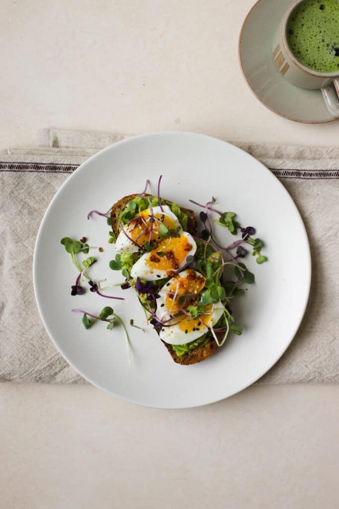 Jammy egg on avocado toast on a plate with matcha on the side.