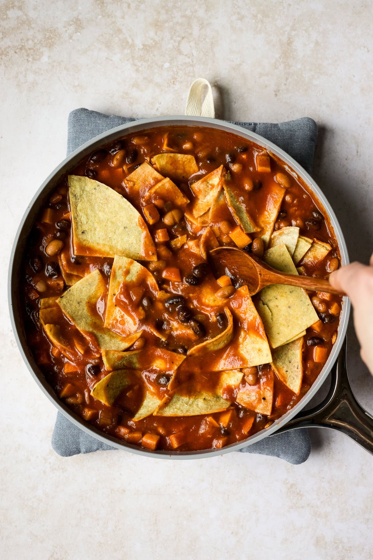 Stirring corn tortillas into skillet enchilada mixture.