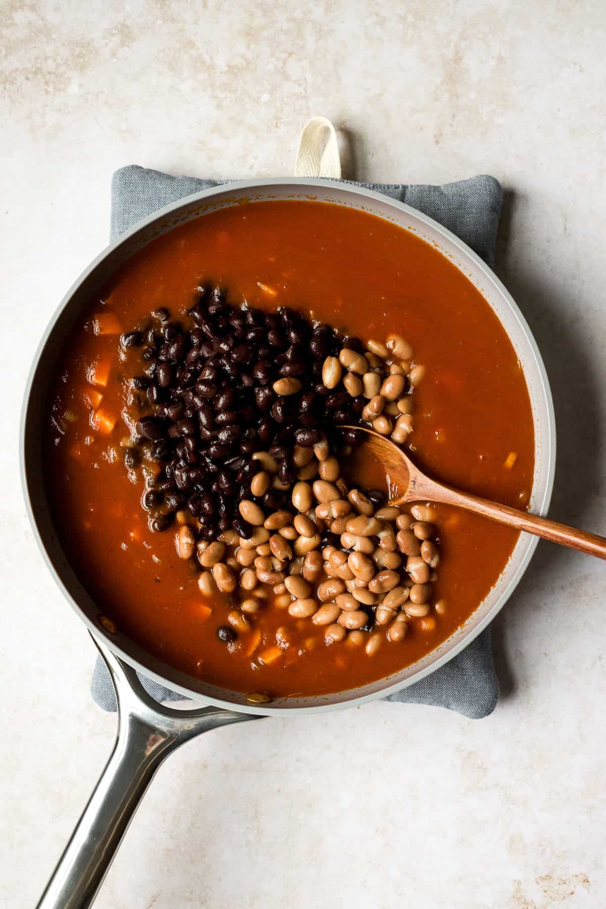 Adding tomato sauce, black beans, and pinto beans to enchilada skillet.