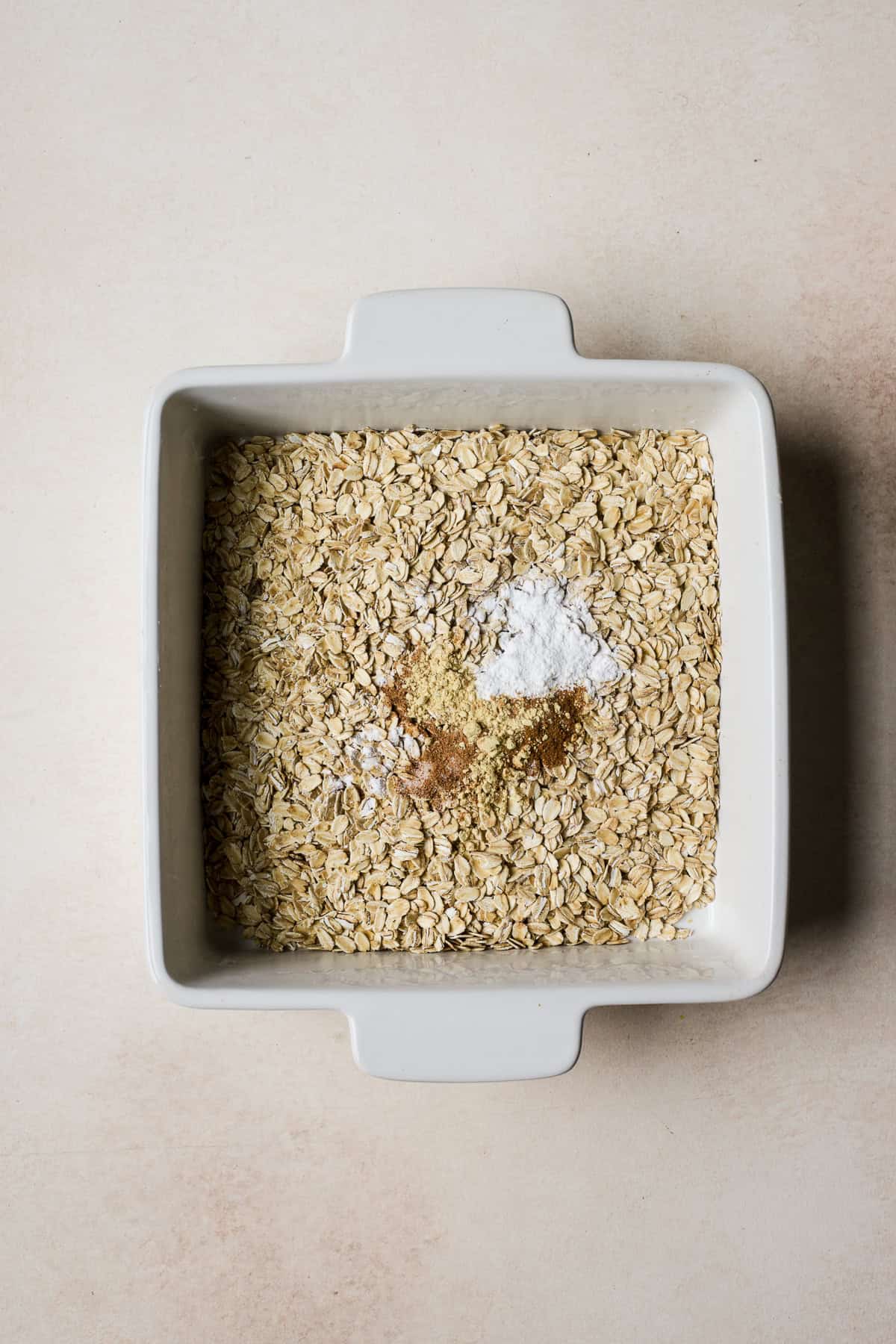 Oats, baking powder, salt, and spices in baking dish for baked oats.